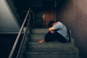 sad man sitting hugging his knees on the stairs of a building